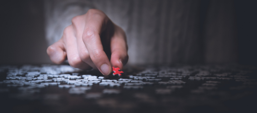 A hand picks up a red puzzle piece in a collection of white pieces.