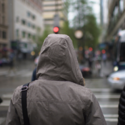 A hooded figure walks through the rain down the street.